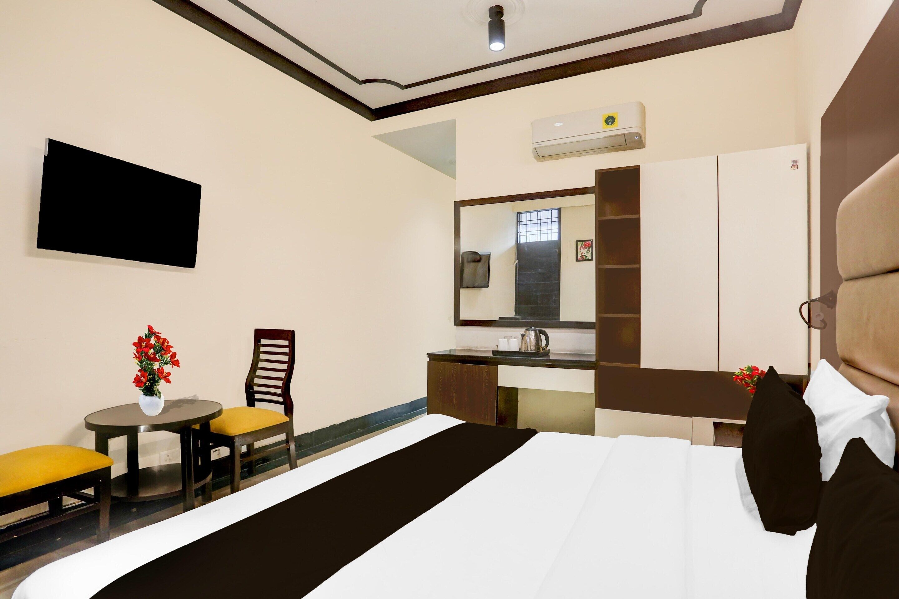 A hotel room with a bed, a small table with chairs, a mirror, and an air conditioning unit.