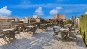 Eine Dachterrasse mit Sitzgelegenheiten im Freien, Blick auf die Stadtlandschaft und wolkenlosen Himmel.