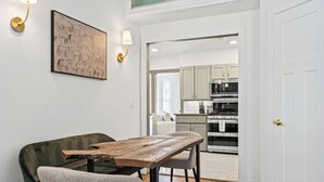 Un comedor con una mesa y sillas de madera, una lámpara de pared y una cocina al fondo.