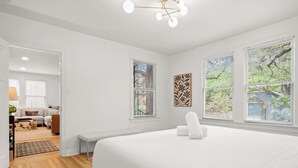Un dormitorio con una cama grande, un banco y dos ventanas con persianas.