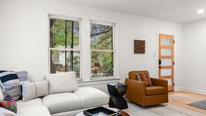 Una sala de estar con un sofá, un sillón marrón, una mesita auxiliar negra y una puerta de madera.