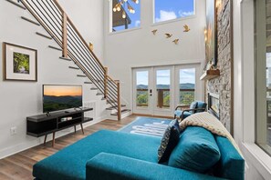 A modern living room with a staircase, a large TV, and a view of the outdoors. - Heavenly Views Hot Tub Games Killer Design (Sevierville)