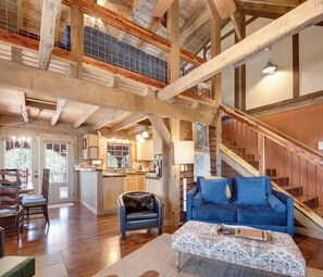 A spacious living area with a high ceiling, wooden beams, a blue sofa, a leather chair, and a kitchen in the background. - Log Cabin Retreat | Spa+BBQ+Hammocks+Dogs+Games (Sevierville)