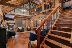 L’intérieur d’une cabane en rondins, avec une cheminée, un escalier en bois et un téléviseur.