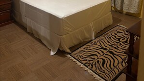A single bed with a wooden headboard, a zebra-patterned rug, and a window with patterned curtains. - Danny's Place in Kingsland Christ Church (Christ Church)