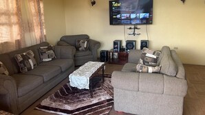 A living room with two sofas, a coffee table, a TV mounted on the wall, and a speaker system. - Danny's Place in Kingsland Christ Church (Christ Church)