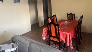 A dining area with a red tablecloth, wooden chairs, a sofa, and a door leading to another room. - Danny's Place in Kingsland Christ Church (Christ Church)