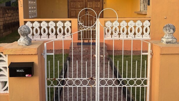A gated entrance to a building with a mailbox, a door with decorative panels, and a small window with bars. - Danny's Place in Kingsland Christ Church (Christ Church)