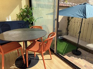 Eine Terrasse mit rundem Tisch und orangefarbenen Stühlen, ein kleiner Garten und ein blauer Sonnenschirm.