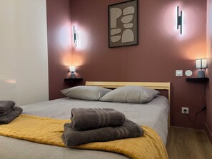 Ein ordentlich bezogenes Bett mit Kissen und Decke, Nachttischlampen, einem an der Wand befestigten abstrakten Kunstwerk und einem hölzernen Kopfteil.