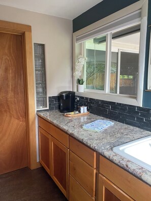A kitchen with a window, wooden cabinets, a countertop, and a coffee maker. - Eugene Friendly Street Neighborhood Retreat (Eugene)