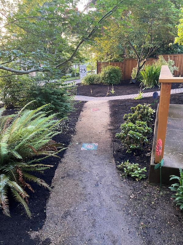 A garden pathway with a speed limit sign, surrounded by various plants and a wooden fence.