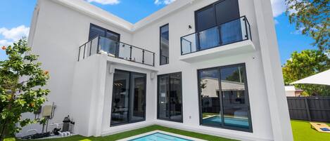 A modern two-story house with a swimming pool, large windows, and a fenced backyard.