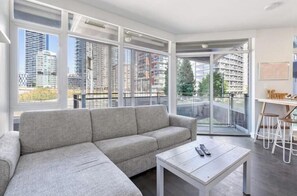 Ein modernes Wohnzimmer mit einem grauen Sofa, einem kleinen Tisch und einem Balkon mit Glastür.