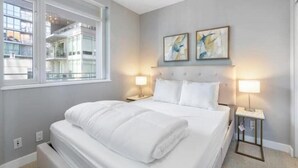 Habitación de hotel con cama, dos lámparas de noche, una ventana y arte abstracto en la pared.