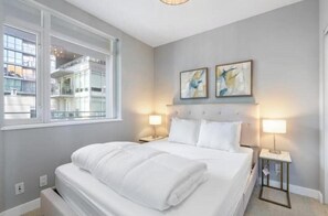 Ein Hotelzimmer mit einem Bett, zwei Nachttischlampen, einem Fenster und abstrakter Kunst an der Wand.
