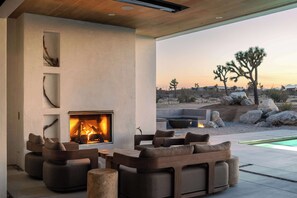 Un espacio al aire libre con mobiliario para sentarse, una chimenea, sofás y vistas al paisaje desértico.