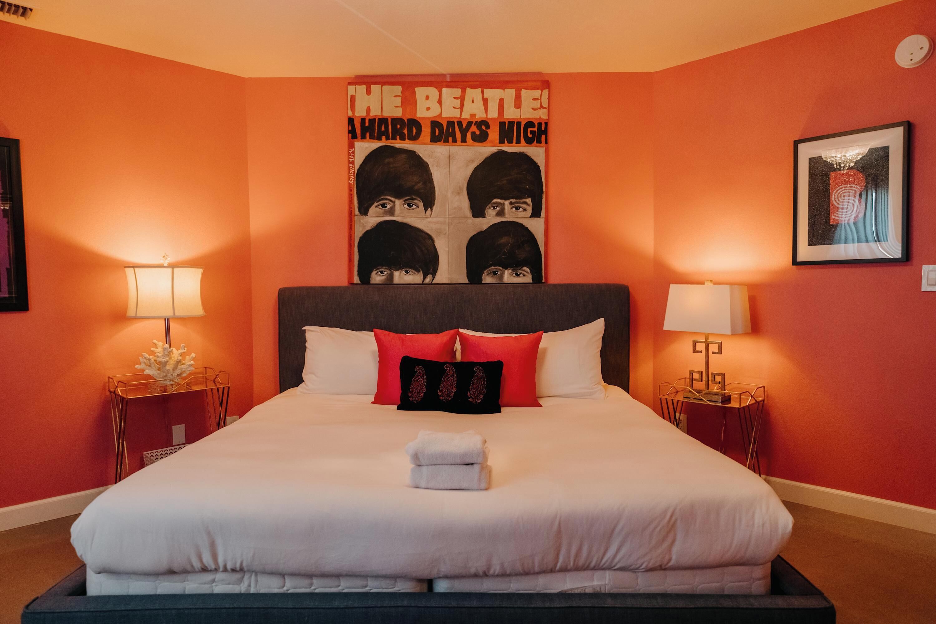 Quarto de hotel com uma cama grande, duas mesas de cabeceira, um cartaz na parede e uma obra de arte emoldurada sobre a cama.