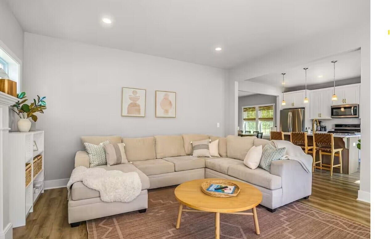 A modern living room with a sectional sofa, a round coffee table, and a kitchen area in the background.