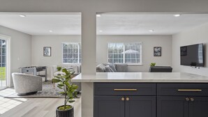 A modern kitchen with a marble countertop, dark cabinets, and a flat-screen TV mounted on the wall. - Relaxing Poolside Haven in Citrus Heights (Citrus Heights)