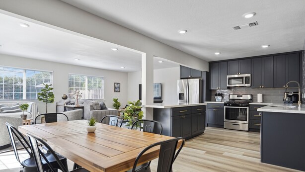 A modern kitchen with dark cabinets, stainless steel appliances, and a wooden dining table. - Relaxing Poolside Haven in Citrus Heights (Citrus Heights)