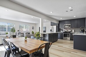 A modern kitchen with dark cabinets, stainless steel appliances, and a wooden dining table.