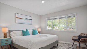 A modern bedroom with a bed, bedside tables, a chair, a window with blinds, and a painting on the wall. - Relaxing Poolside Haven in Citrus Heights (Citrus Heights)