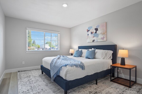 A bedroom with a bed, bedside lamps, a window, and a painting on the wall.