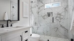 A bathroom with a white sink, a mirror, a toilet, and a shower with marble walls. - Relaxing Poolside Haven in Citrus Heights (Citrus Heights)