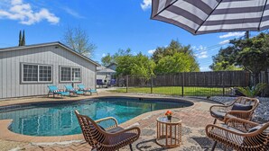 A backyard with a swimming pool, wicker chairs, a patio umbrella, and a fenced area. - Relaxing Poolside Haven in Citrus Heights (Citrus Heights)