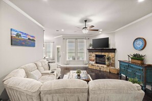 A living room with a sectional sofa, a fireplace, a television, and a ceiling fan. - Heart of Ferris: 3-BD/2-BA with Pool, Patio & BBQ (Ferris)