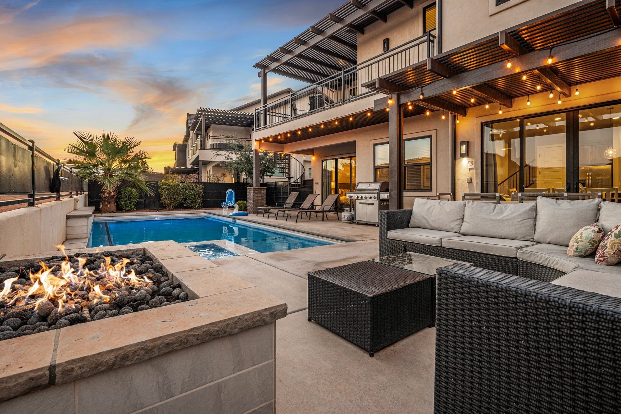 A pool area with a fire feature, outdoor seating, and a barbecue grill.