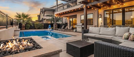 A pool area with a fire feature, outdoor seating, and a barbecue grill.
