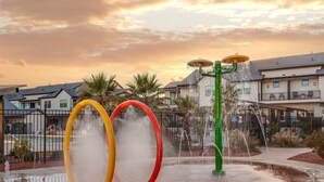 A water feature with three colorful rings and a green structure in a courtyard with residential buildings in the background. - Ocotillo Springs 53, Private Pool, Spa, Resort Amenities (Santa Clara)