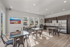 Eine moderne Küche mit Edelstahlkühlschrank, Holzschränken und einem Essbereich mit Glastischen und -stühlen.