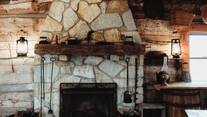 Une cheminée rustique en pierre, surmontée d’une manteau en bois, entourée de murs en pierre et de poutres apparentes.