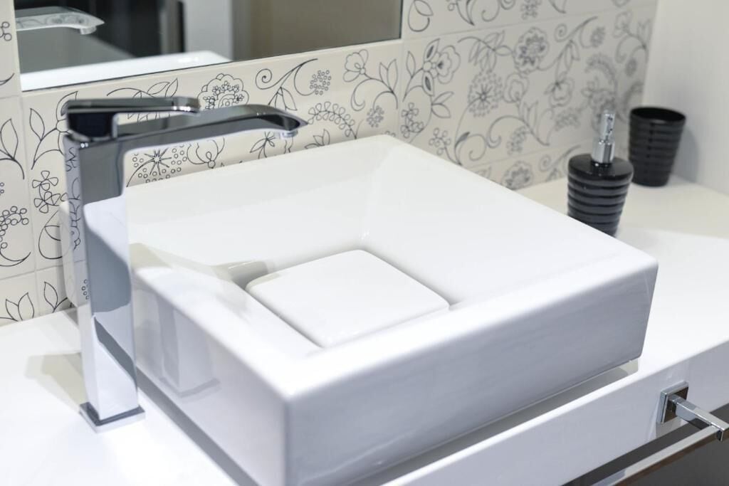 A modern bathroom with a white square sink, a chrome faucet, and a decorative mirror.