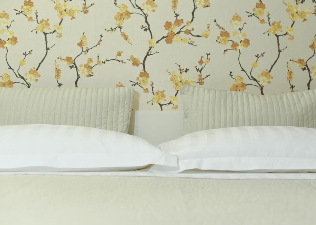 Una cama con ropa de cama blanca y un estampado floral en la pared.
