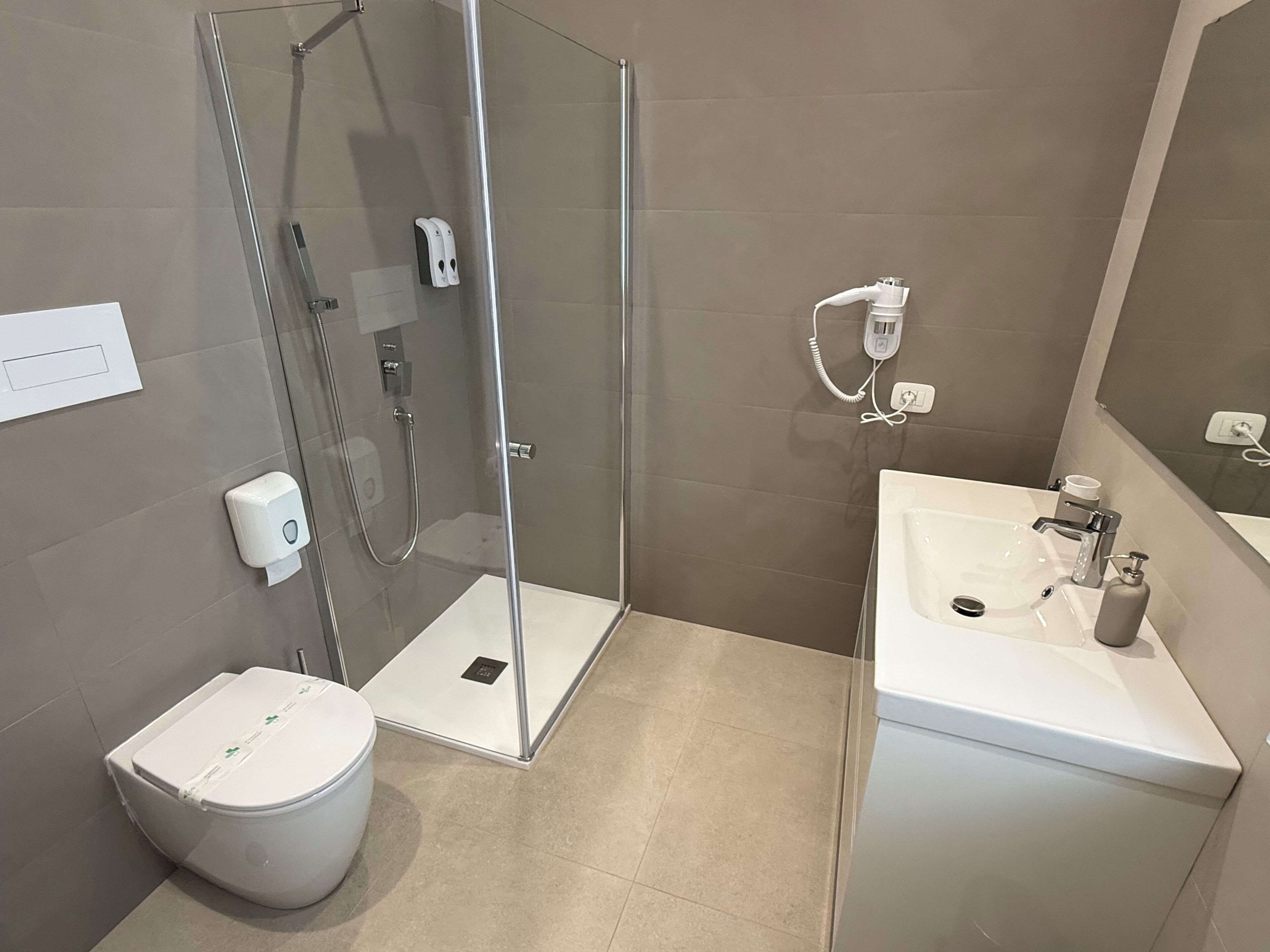 A modern bathroom with a glass-enclosed shower, a toilet, and a sink with a mirror.
