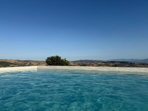 A clear blue pool with a view of a distant landscape and a tree. - Giardini Hurz (Pietrelcina)
