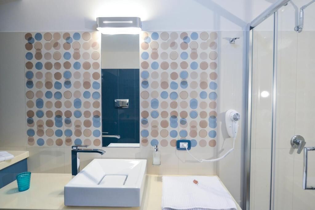 Un baño con lavamanos blanco, espejo, toalla y zona de ducha.