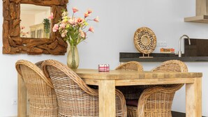 Ein Essbereich mit Korbstühlen, einem Holztisch, einer Vase mit Blumen, einem Spiegel und einer Küchenspüle.