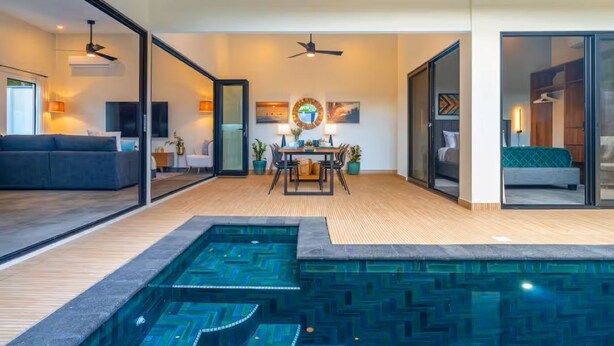 Un soggiorno moderno con piscina, zona pranzo e una camera da letto visibili attraverso porte in vetro.