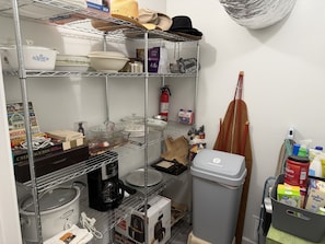 Una cocina con estantes que contienen diferentes utensilios, una cafetera y un cubo de basura.