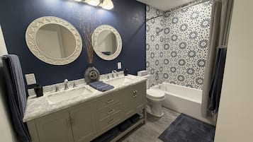 A bathroom with a double sink vanity, a toilet, a bathtub, and a shower area.