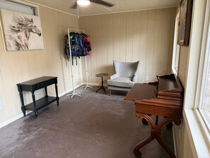 A room with a wooden floor, a black table, a grey armchair, a wooden desk, and a coat rack with clothes. - Cowboy On The Water at Lake Palo Pinto. Private Dock, New Remodel. Howdy Y'all. (Gordon)