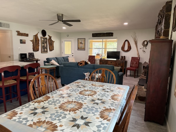 Una sala de estar con un sofá azul, una mesa de comedor con mantel estampado y un ventilador de techo.