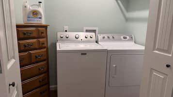 Une buanderie avec un lave-linge et un sèche-linge blancs, une commode en bois avec des tiroirs, et une bouteille de lessive Tide posée sur le dessus.