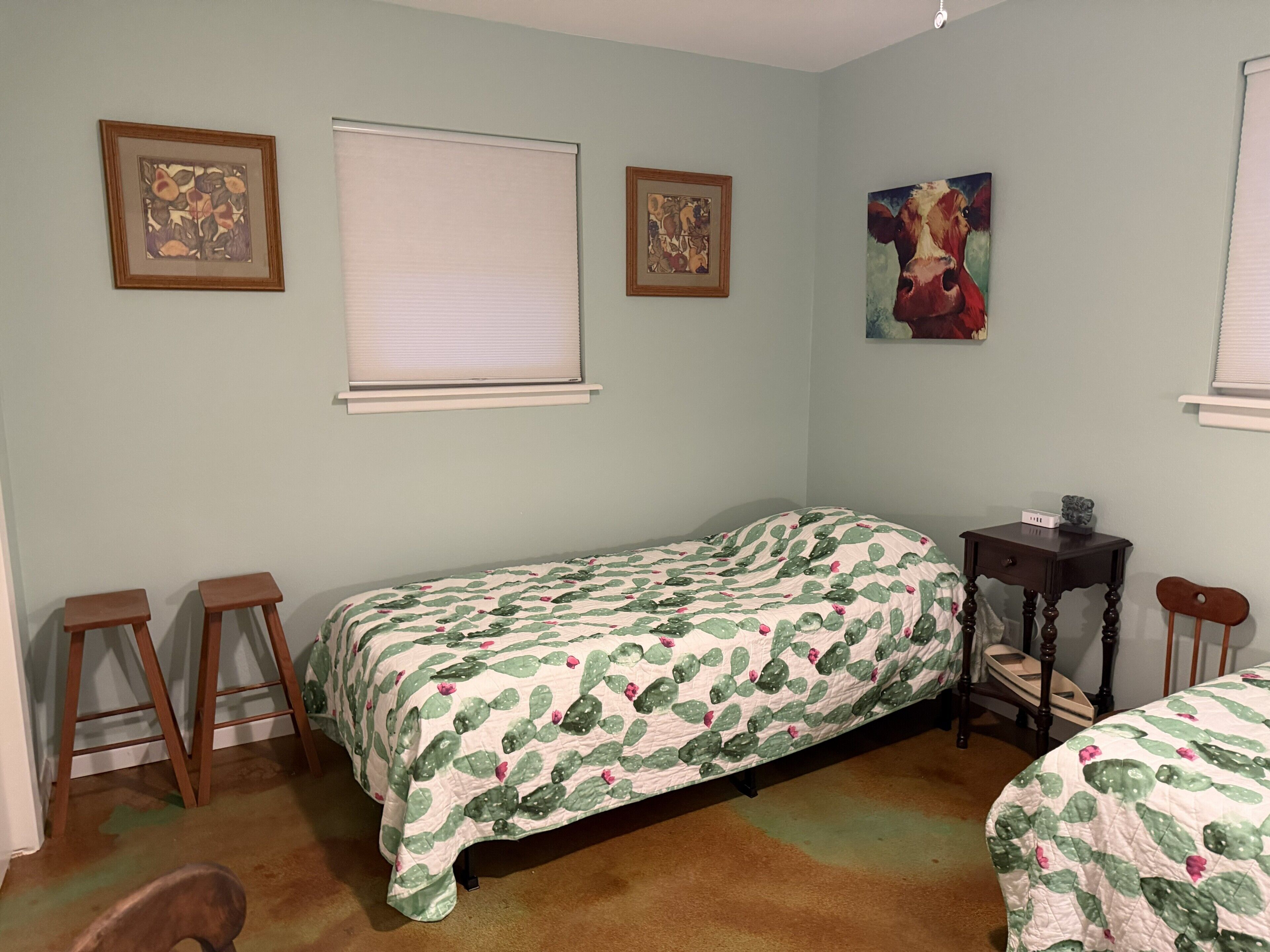 A bedroom with a single bed, a nightstand, a chair, and two framed pictures on the wall.