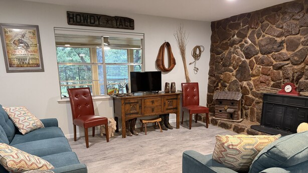 A cozy living room with a stone wall, a fireplace, a television, and a desk with chairs. - Cowboy On The Water at Lake Palo Pinto. Private Dock, New Remodel. Howdy Y'all. (Gordon)